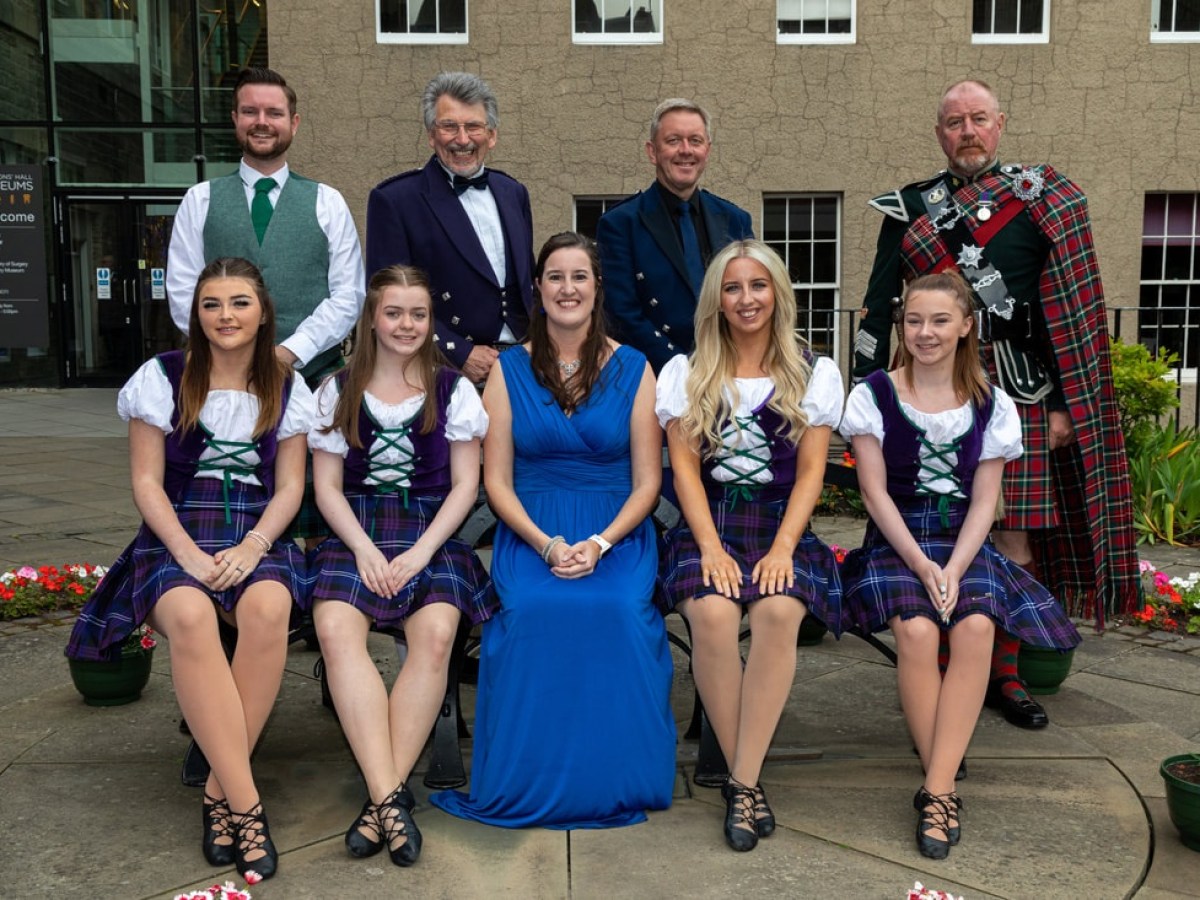 Group photo of six women in traditional attire and three men in kilts outdoors.