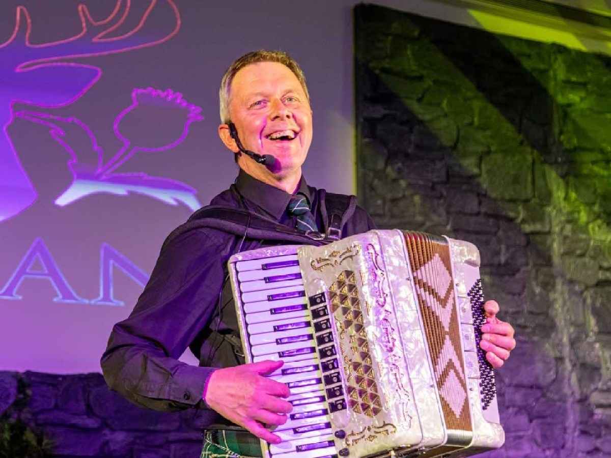 Man in purple shirt playing accordion on stage, smiling.