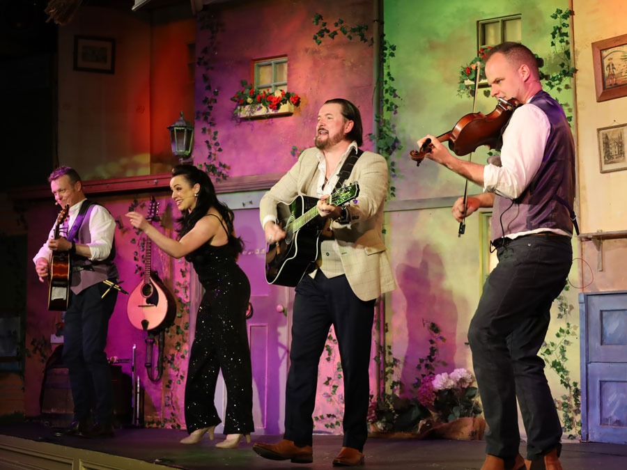 Musicians performing with guitars and violin on a colorful stage.