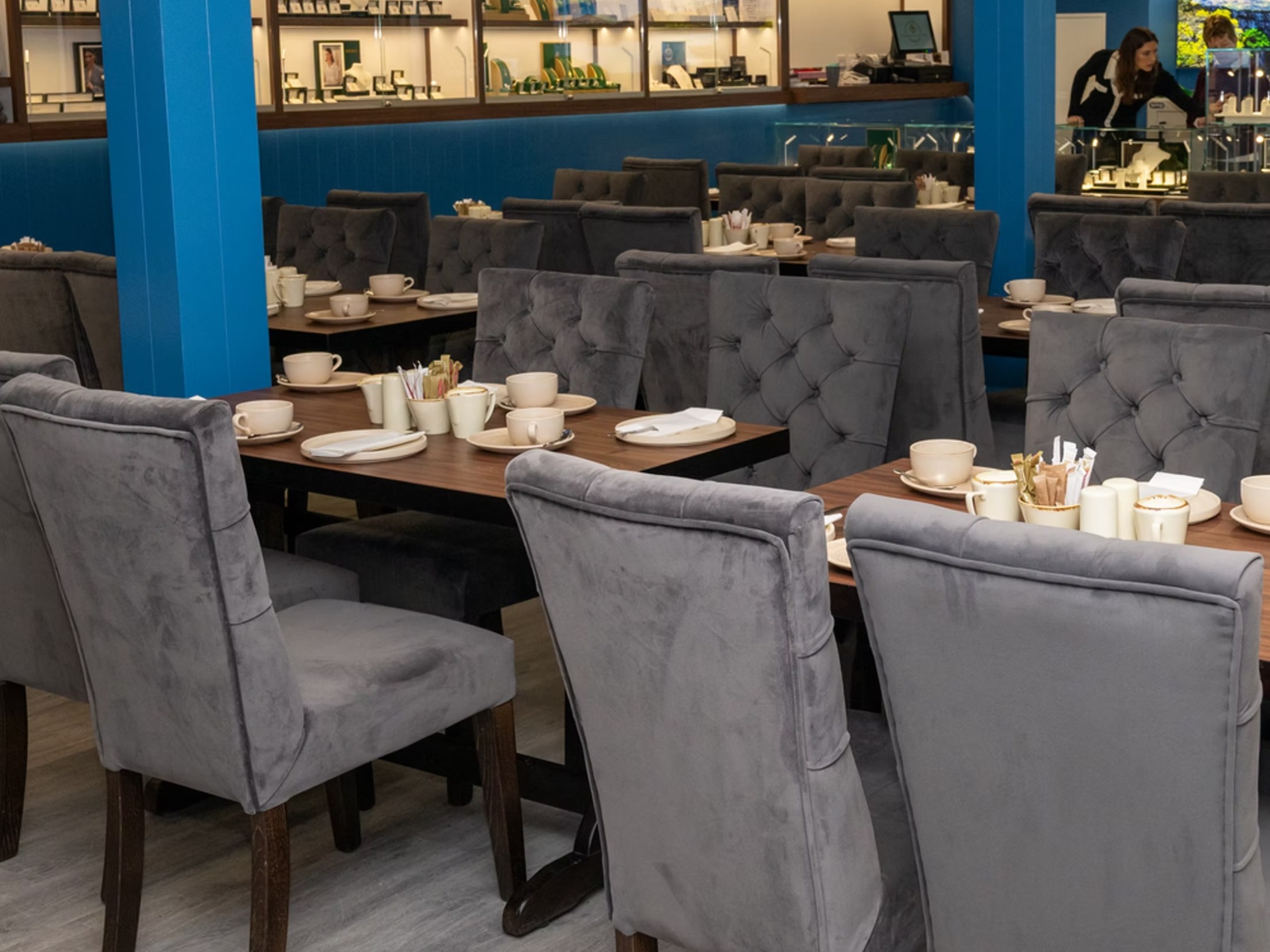 Empty restaurant with grey chairs, set tables, and blue columns.
